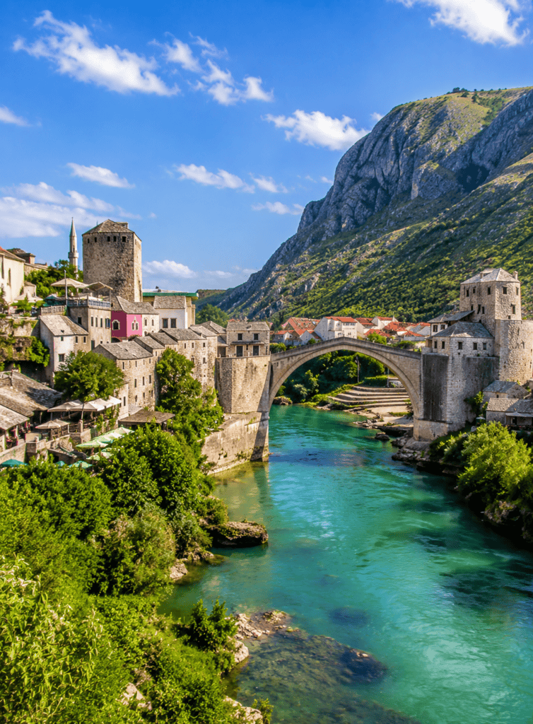 Historic Italian town with a bridge over a turquoise river and mountain backdrop.